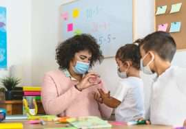 Teacher cleaning hands to student children with sanitizer gel while wearing face mask